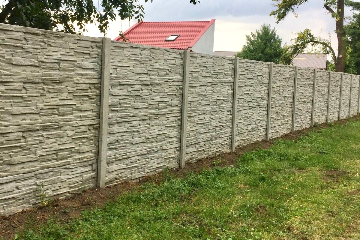 Betonový plot štípaný kámen u domu s červenou střechou