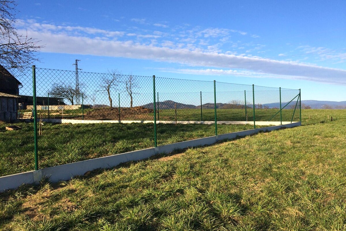 Dlouhý pletivový plot s podhrabovými deskami v krajině